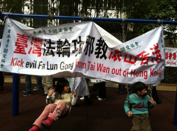 Children are seen playing on a swing from which the Hong Kong Youth Care Association hung a banner attacking Falun Gong. In the background, another Association banner is seen on the playlot's fence. In November 2012, the Association began blanketing Hong Kong with banners such as this. (Epoch Times)