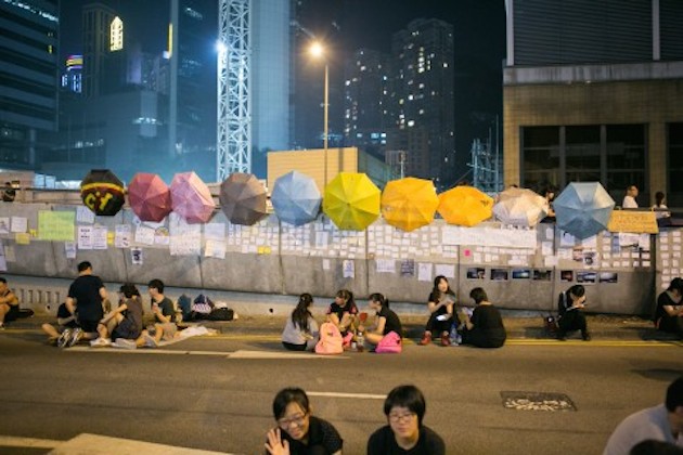 People sit under umbrellas on one of the main roadways near the Government Complex in Hong Kong on October 2, 2014. (Benjamin Chasteen/Epoch Times)
